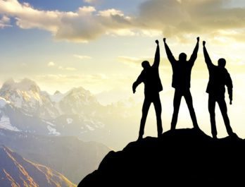three people with their arms raised on top of a mountain