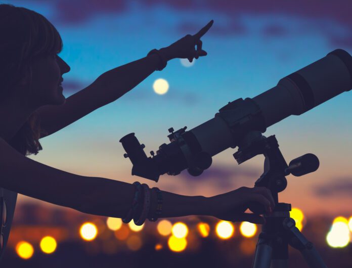 person using a telescope, smiling and pointing toward the night sky