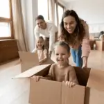 couple pushing young children in moving boxes