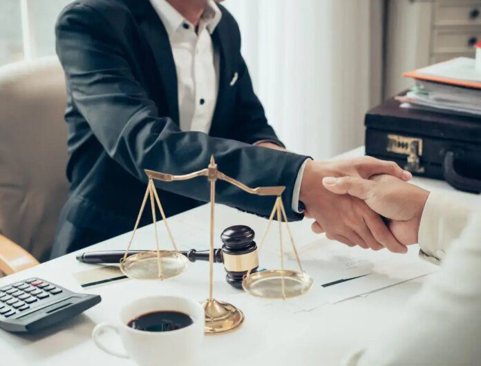Attorney shaking hands with a client at his desk with a cup of coffee, scale, gavel and calculator in the foreground.