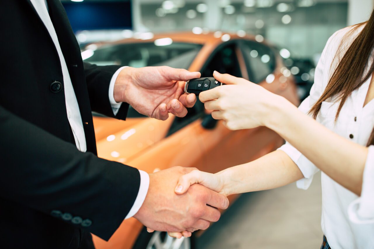 The seller hands over the keys to the buyer on the back of a car dealership.