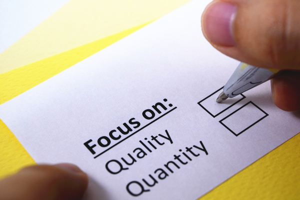 A business card that says "Focus on" with two boxes beneath  to check for quality or quantity. A person with a pen is about to check "quality."