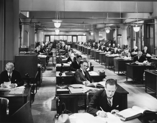 Black and white photo of vintage office with rows of desks.