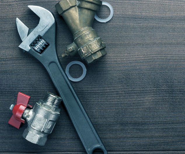 A plumbers wrench and two pipe valves against a wooden background.