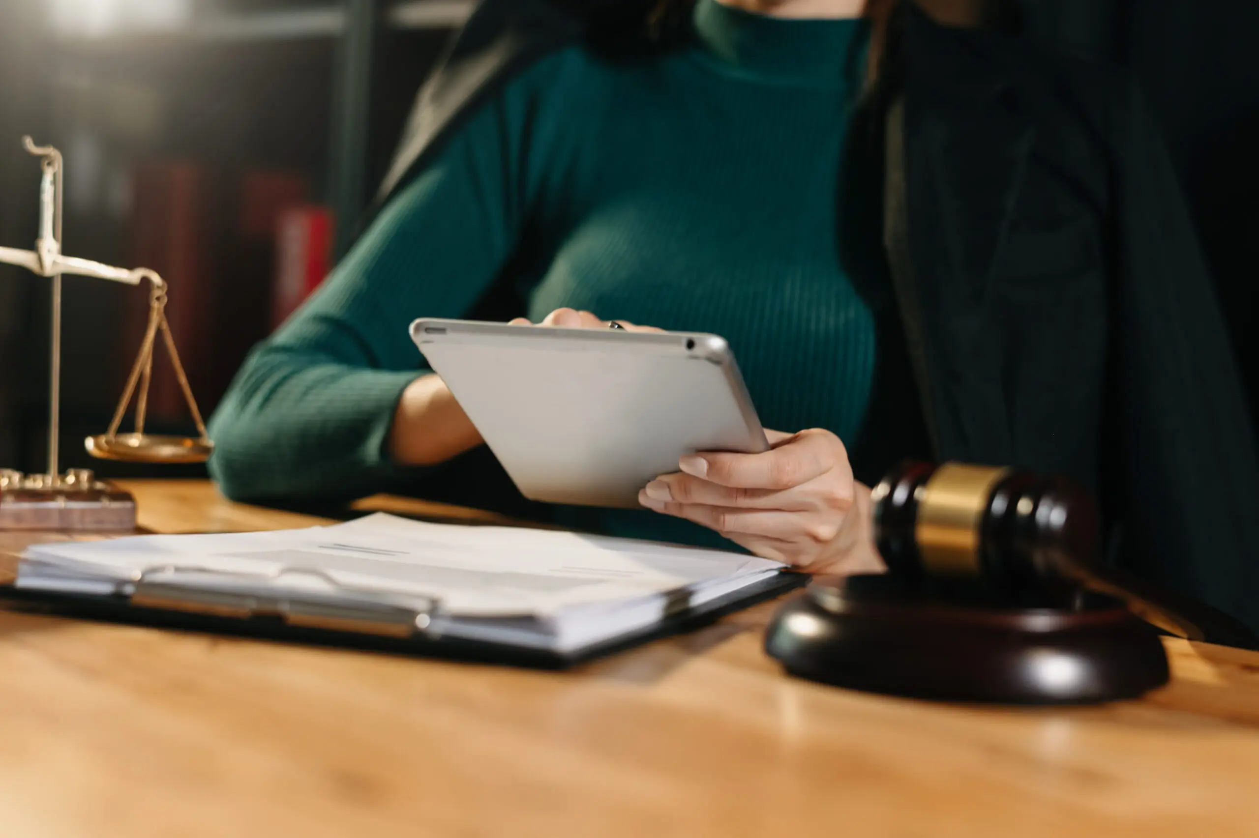 A judge seated at a desk working on a tablet surrounded by a scale, a tablet of paper and a gavel.